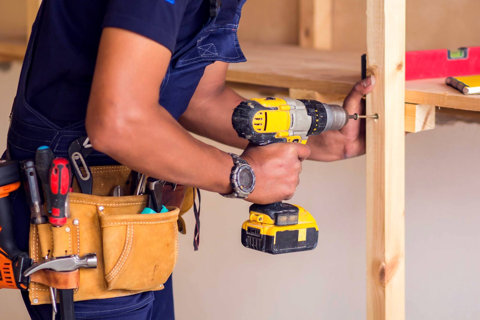 Construction worker using yellow cordless drill on wooden framing