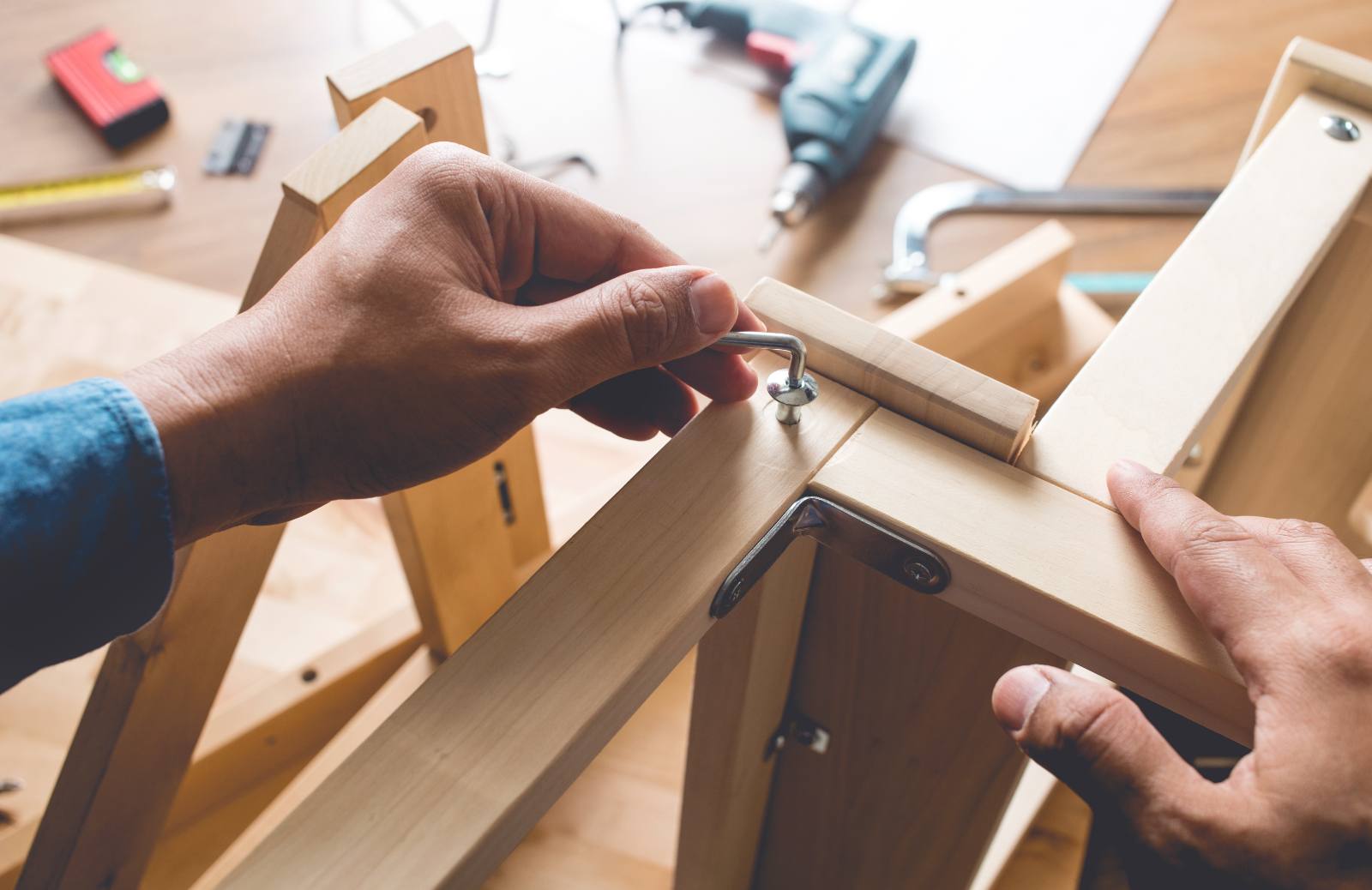 Hands installing a metal hinge on wooden furniture at a workbench