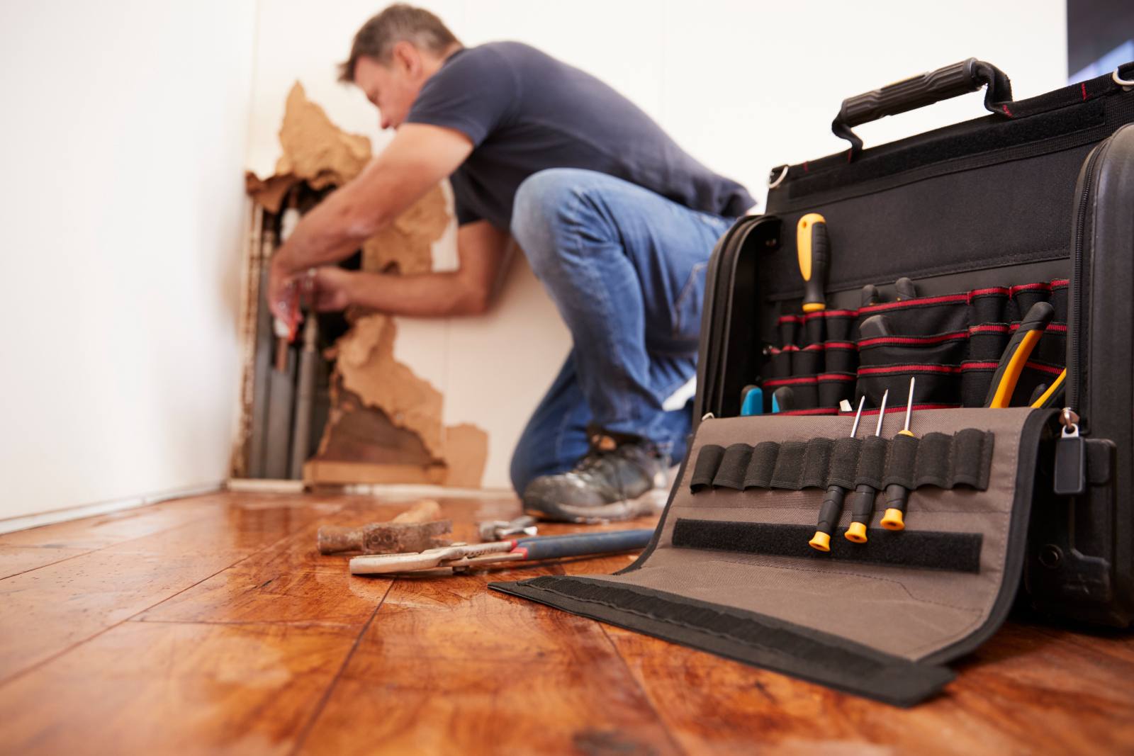 Contractor with open toolbag working on drywall installation indoors