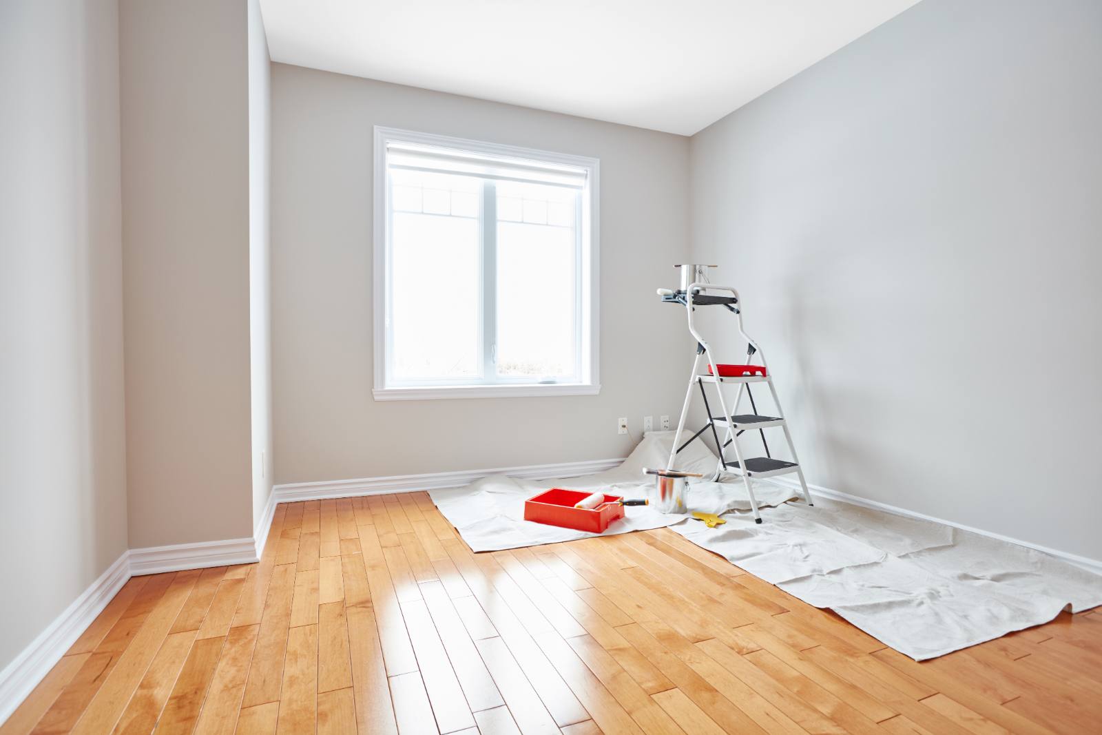 Home interior renovation in progress with ladder, paint supplies, and drop cloths on wooden floor